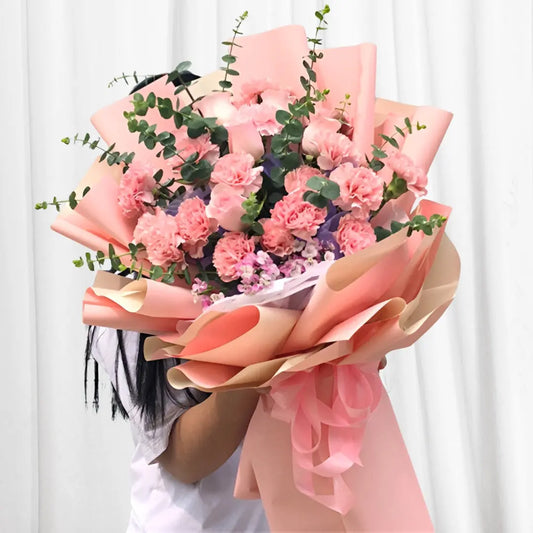 Blossom Serenity Floral Bouquet with pink carnations, light pink roses, stock flowers, and eucalyptus in soft peach wrap.