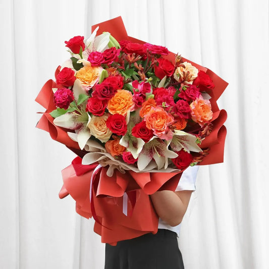 Vibrant Fiesta Rose Bouquet featuring red, orange, and pink roses, white lilies, orange carnations, and alstroemeria with lush greenery.